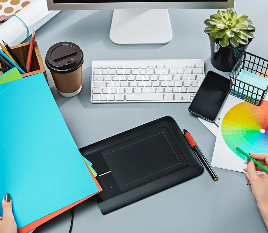 Biurko projektanta graficznego z tabletem, próbnikiem kolorów i akcesoriami do pracy kreatywnej.