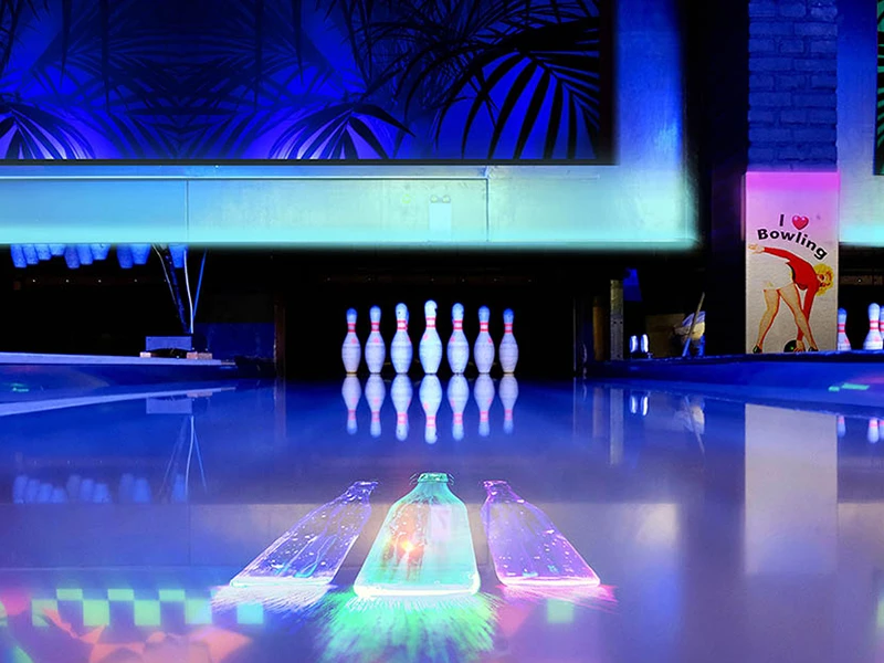 Kręgielnia z oświetlonym torem i ustawionymi na końcu kręglami pod niebieskim światłem.