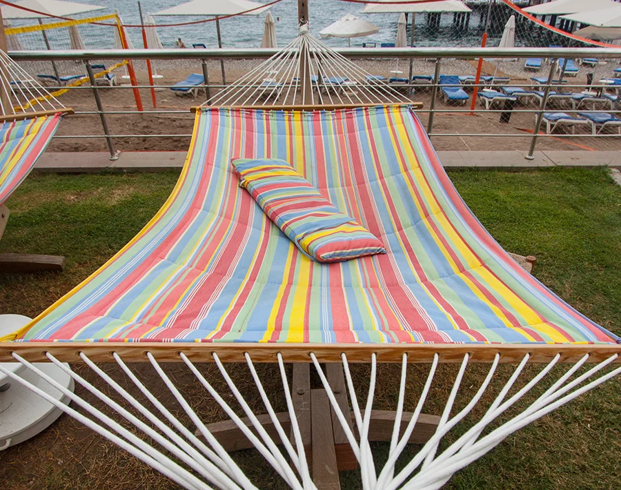Duży, kolorowy hamak w paski rozpięty na metalowej konstrukcji w przestrzeni zewnętrznej.