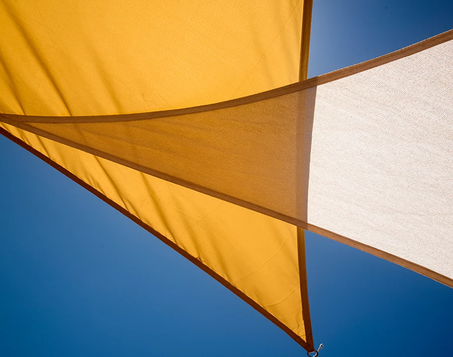 Żółto-biały żagiel słoneczny rozpięty nad przestrzenią zewnętrzną na tle nieba.