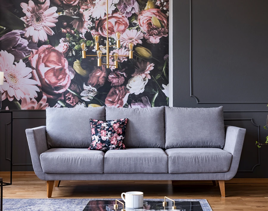 Fototapeta z kwiatowym wzorem zamontowana na ścianie za szarą sofą w salonie.