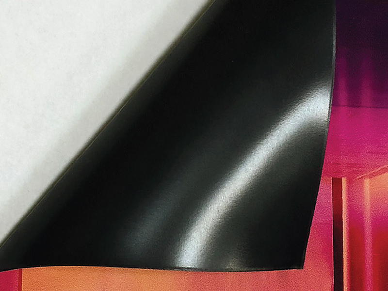 Biała folia magnetyczna z czarnym, elastycznym spodem, lekko odgięta, ukazująca warstwę magnetyczną.