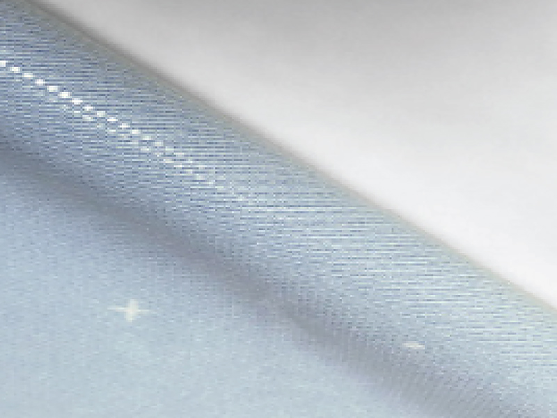 Biały materiał Dotcor z drobną, punktową strukturą powierzchni, lekko podwinięty.