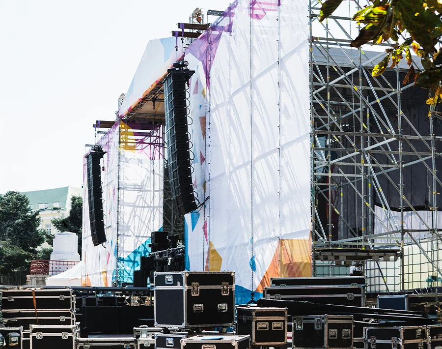 Biały baner osłaniający konstrukcję sceniczną i głośniki podczas wydarzenia plenerowego.