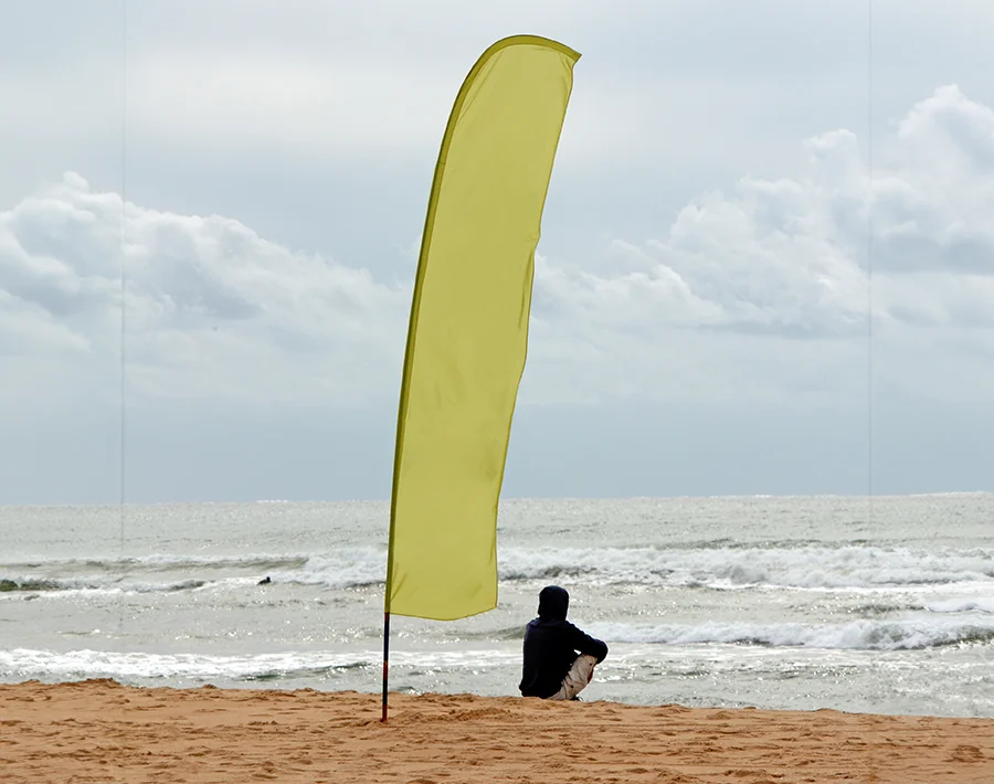 Żółta flaga plażowa typu skrzydło ustawiona na piasku nad brzegiem morza.