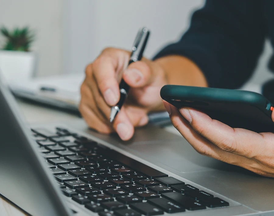 Osoba trzymająca kartę płatniczą i telefon przy laptopie podczas zakupów online.