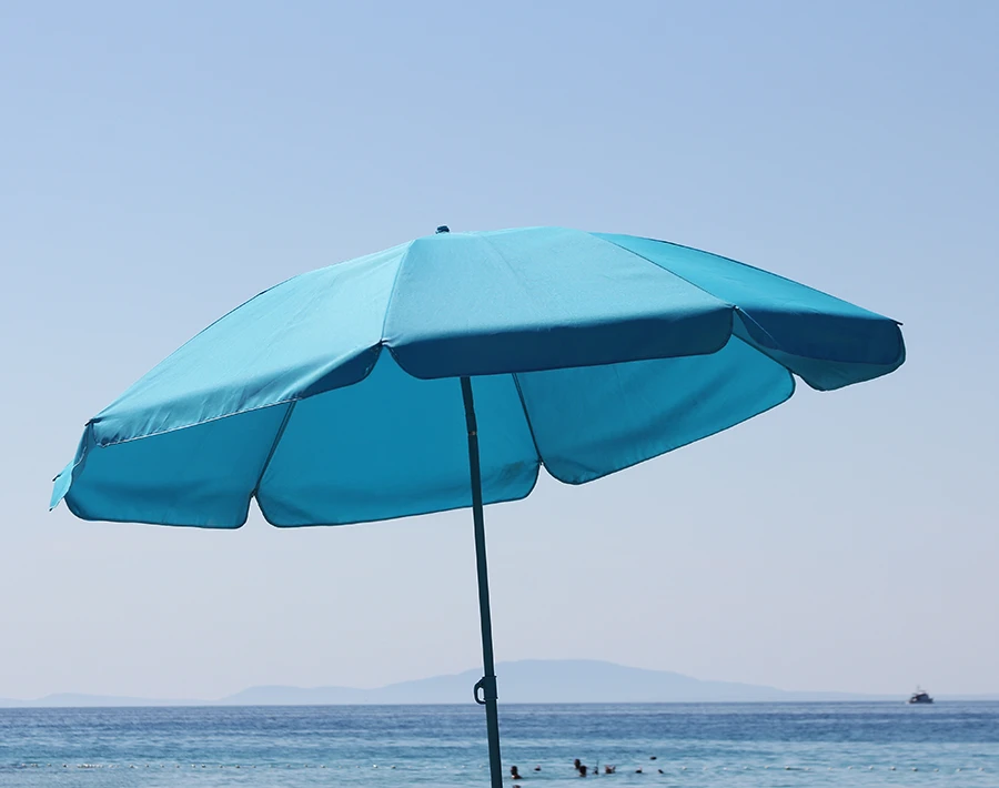 Niebieski parasol reklamowy rozłożony nad plażą z widokiem na morze w tle.