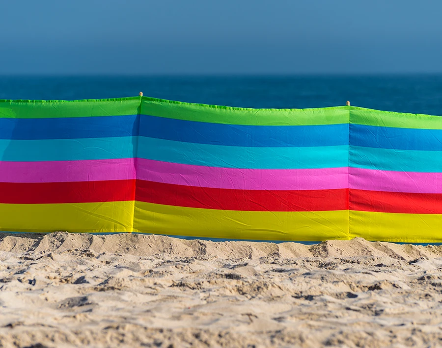 Kolorowy parawan plażowy w poziome pasy ustawiony na piasku nad morzem.