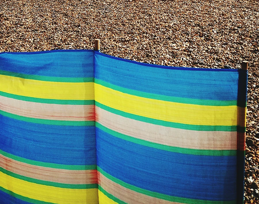 Kolorowy parawan plażowy w pasy ustawiony na kamienistej plaży.