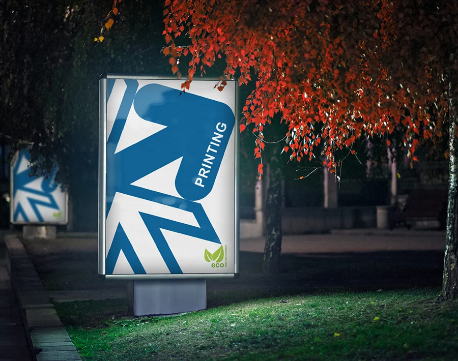 Podświetlany nośnik reklamowy z niebiesko-białą grafiką ustawiony w przestrzeni miejskiej nocą.