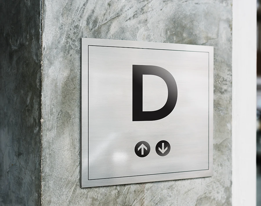 Biała tablica reklamowa z oznaczeniem litery „D”, zamocowana na ścianie budynku.