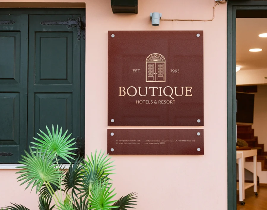 Biała tablica reklamowa z nadrukiem logo i nazwą boutique, zamocowana przy wejściu do lokalu.