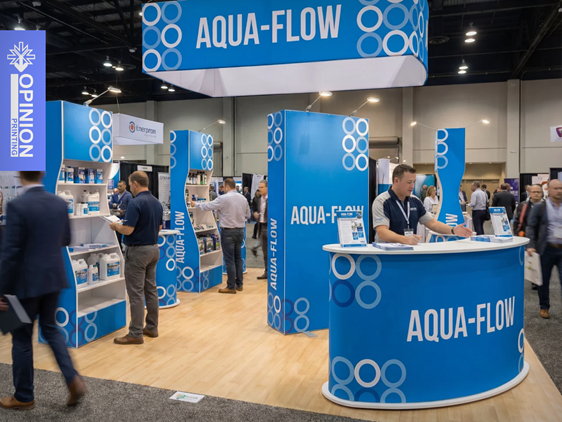 Białe stoisko targowe z ladą i zabudową ekspozycyjną prezentowane podczas wydarzenia branżowego w hali wystawienniczej.